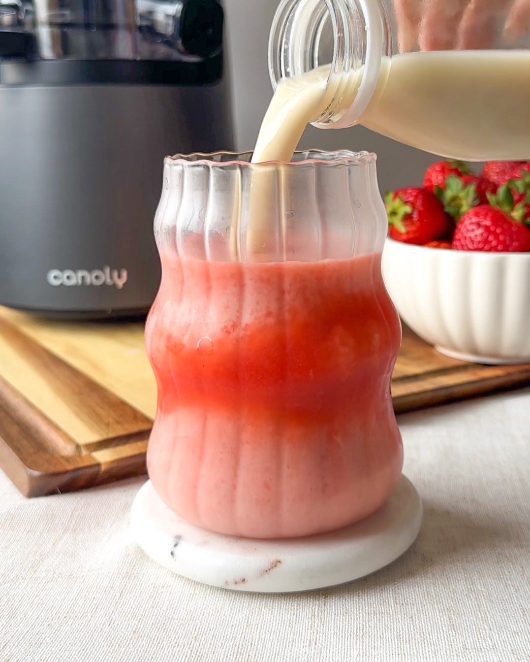oat milk being poured into glass to make strawberry. milk with a canoly juicer in the background