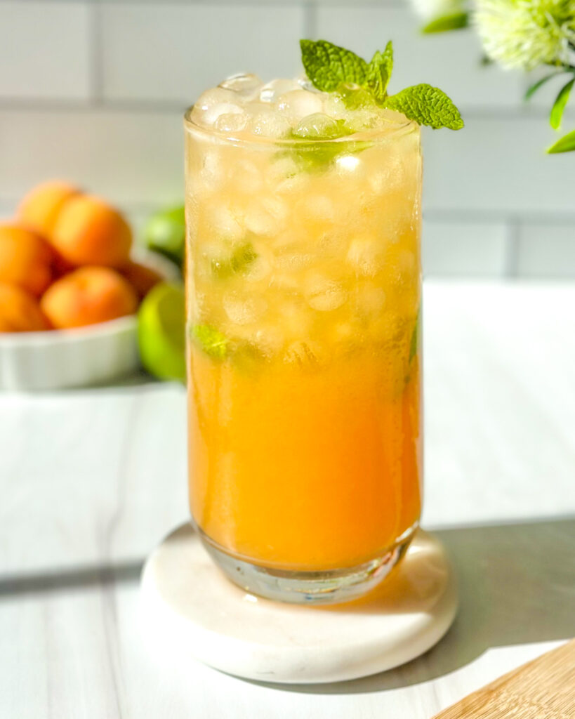 Fresh apricot mojito recipe garnished with mint, served over ice with apricots and limes in the background