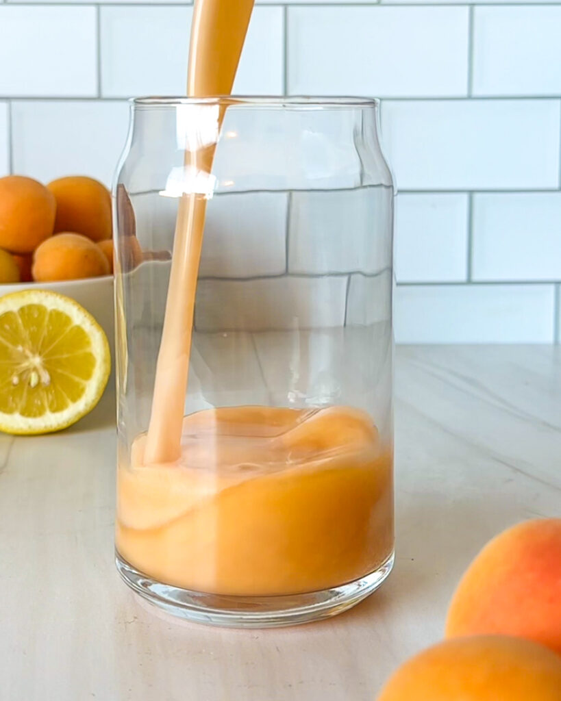 Homemade apricot lemonade being poured into a chilled glass, showing its smooth, vibrant texture as it fills the glass.