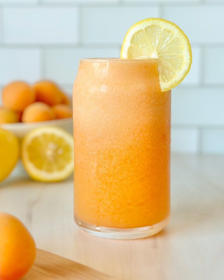 Two glasses of fresh apricot lemonade served chilled, styled with apricots and sliced lemon in the background for a bright summer drink scene.