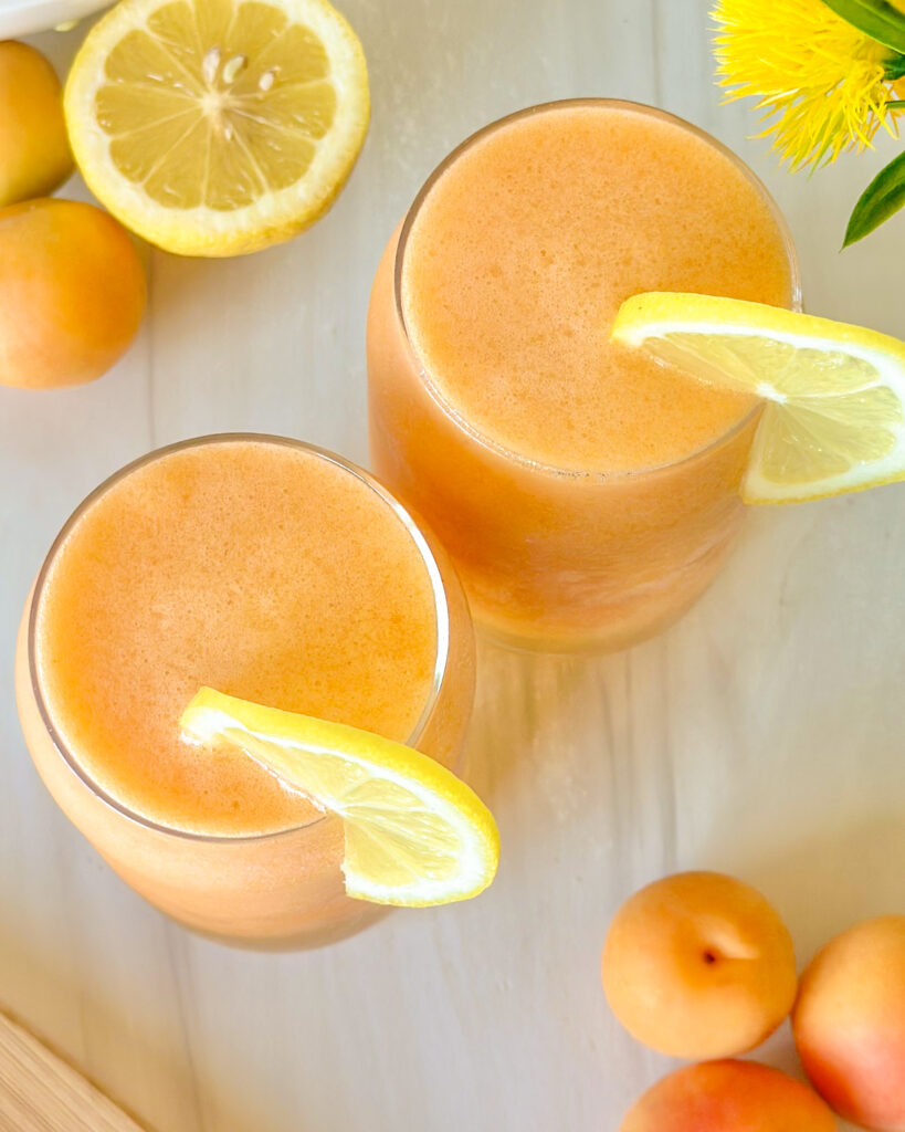 Top-down view of two glasses of apricot lemonade showing a frosty, ice-cold texture, styled with fresh apricots and lemon for a refreshing summer feel.