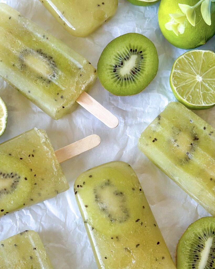 Close-up detail of kiwi popsicles on baking paper with fresh kiwi and lime slices.