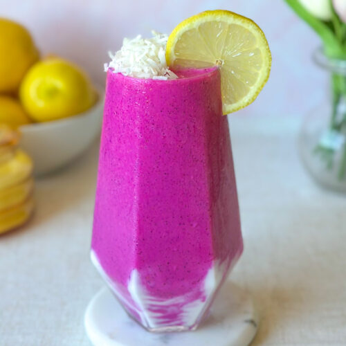 Vibrant pink dragon fruit smoothie with a creamy yogurt swirl, shredded coconut, and fresh lemon garnish