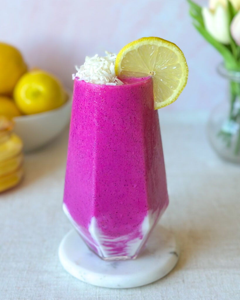 Vibrant pink dragon fruit smoothie with a creamy yogurt swirl, shredded coconut, and fresh lemon garnish
