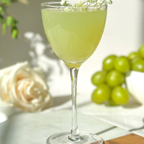 Green grape gimlet cocktail in coupe glass eith fresh green graoes and floral garnish
