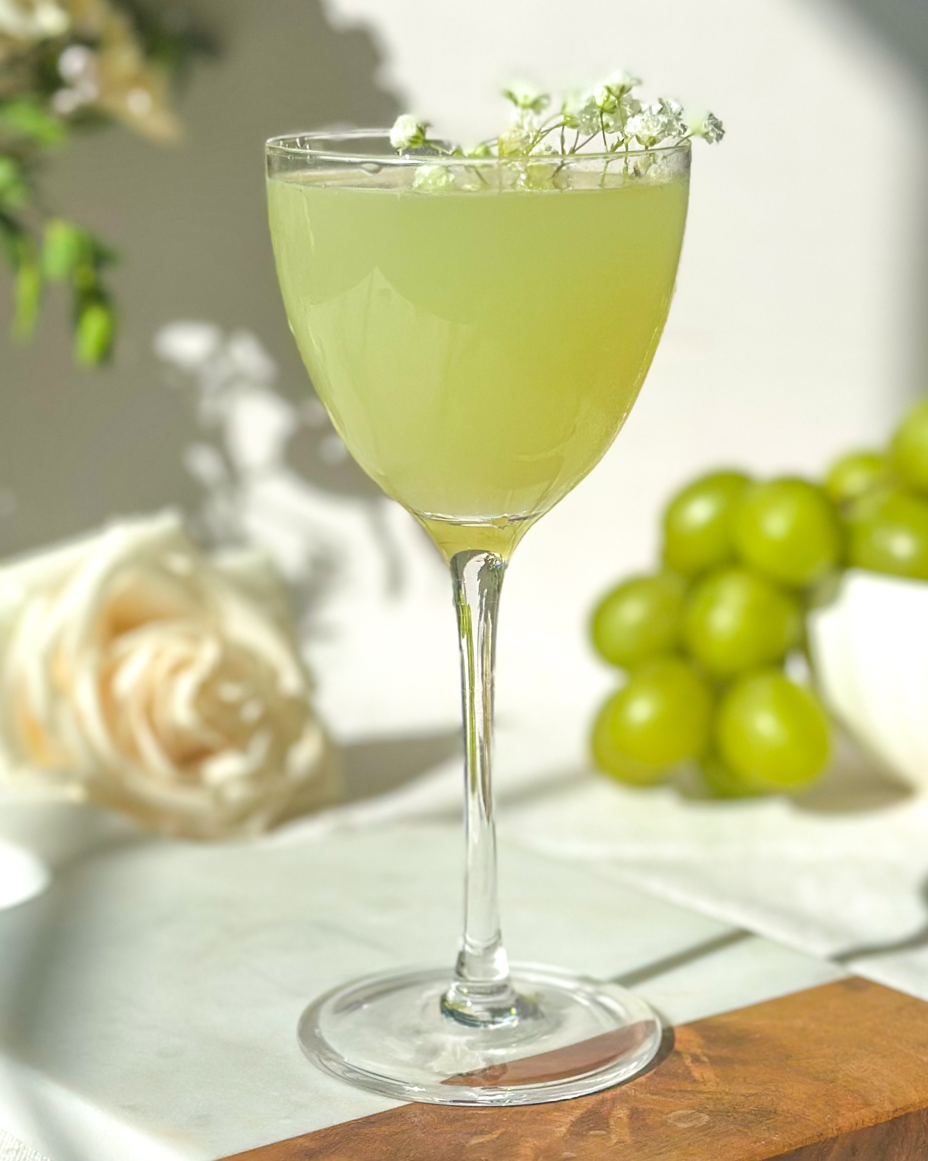 Green grape gimlet cocktail in coupe glass eith fresh green graoes and floral garnish