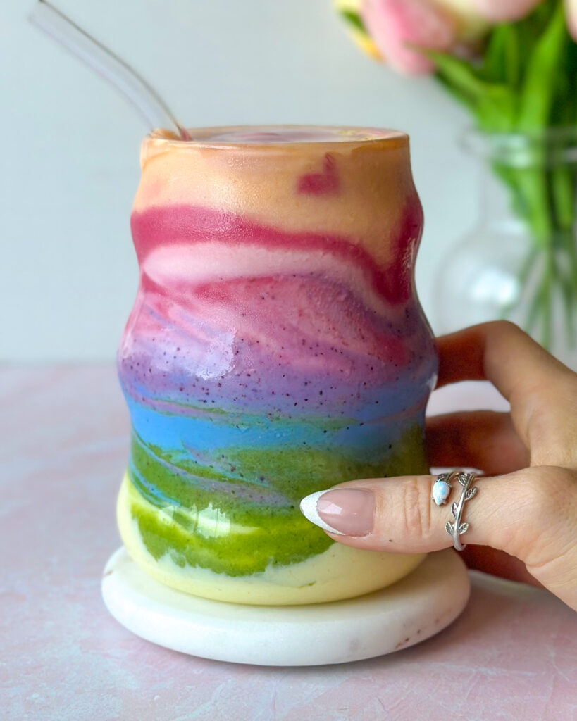 Hand holding a seven layer rainbow smoothie with vibrant natural colors
