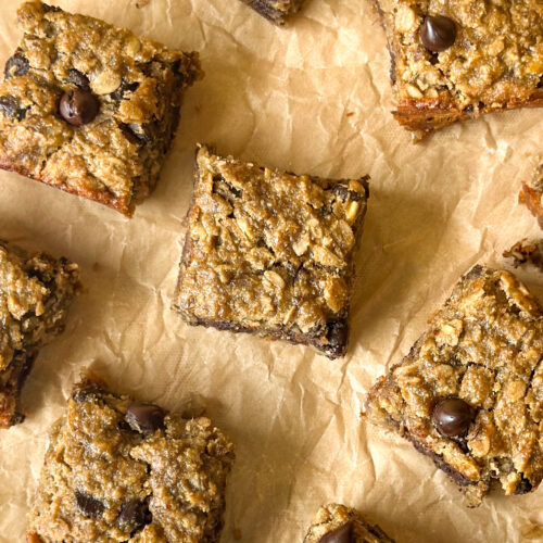 Baked banana oat chocolate chip bars spread across baking paper, filling the frame with golden brown chewy squares