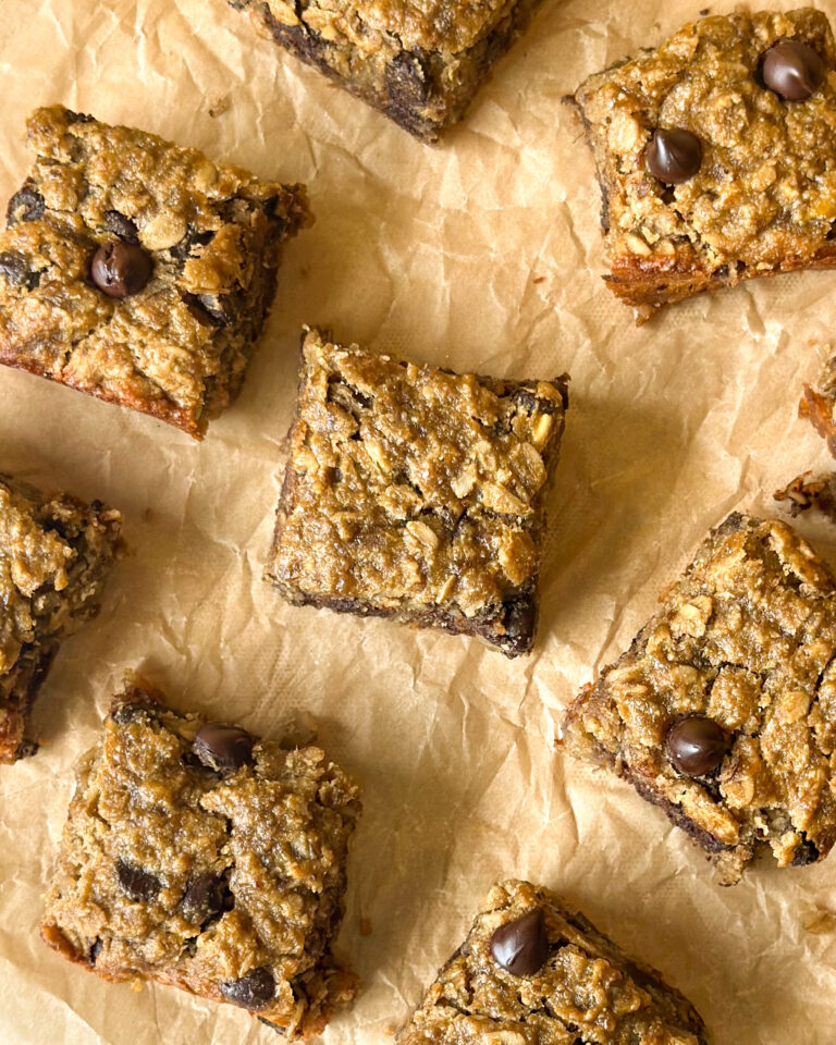 Baked banana oat chocolate chip bars spread across baking paper, filling the frame with golden brown chewy squares