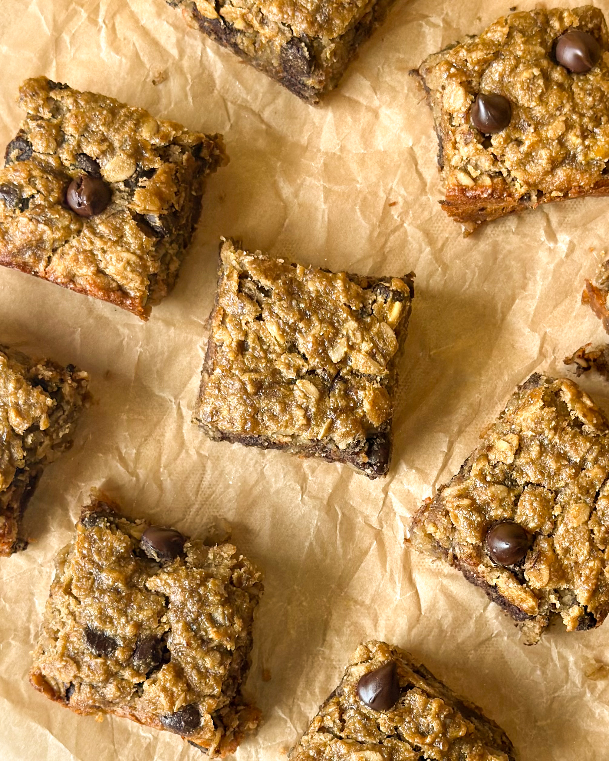 Baked banana oat chocolate chip bars spread across baking paper, filling the frame with golden brown chewy squares