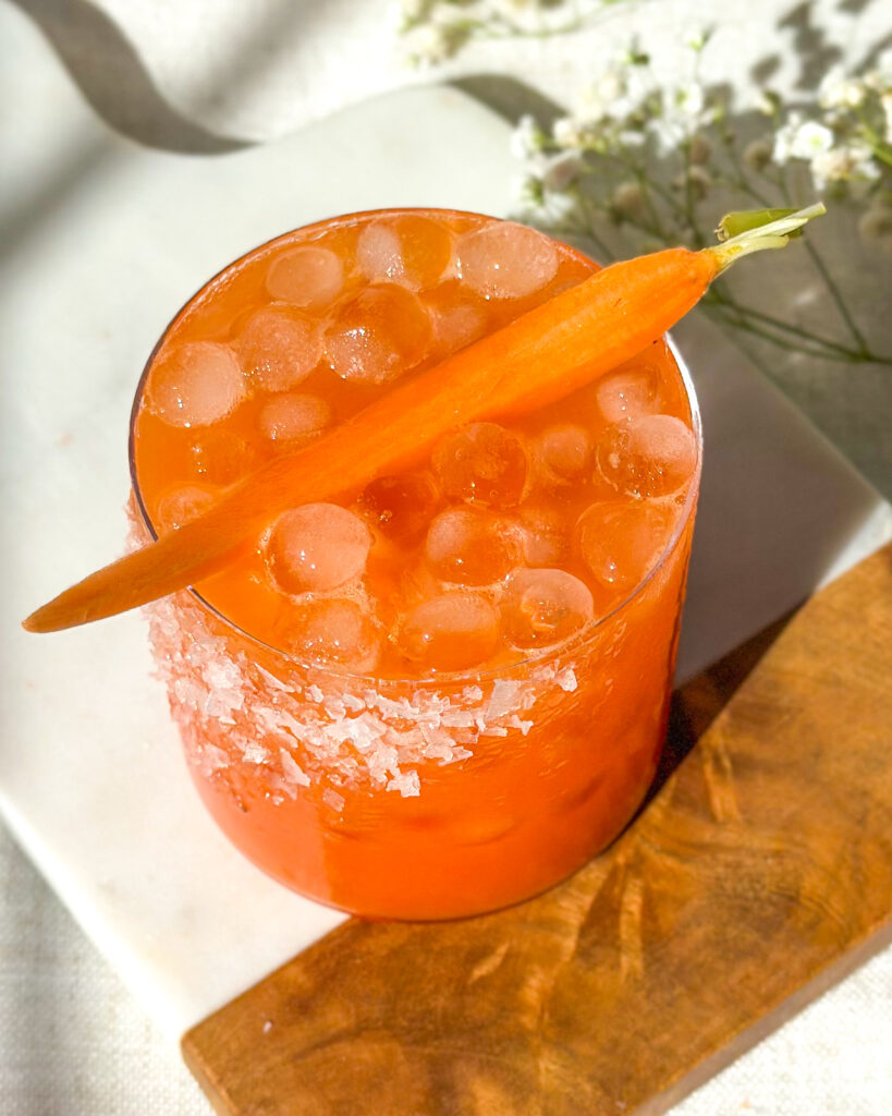 Overhead top-down view of a strawberry carrot margarita highlighting the salted rim, ice, and vibrant orange color of the cocktail in a styled setting.