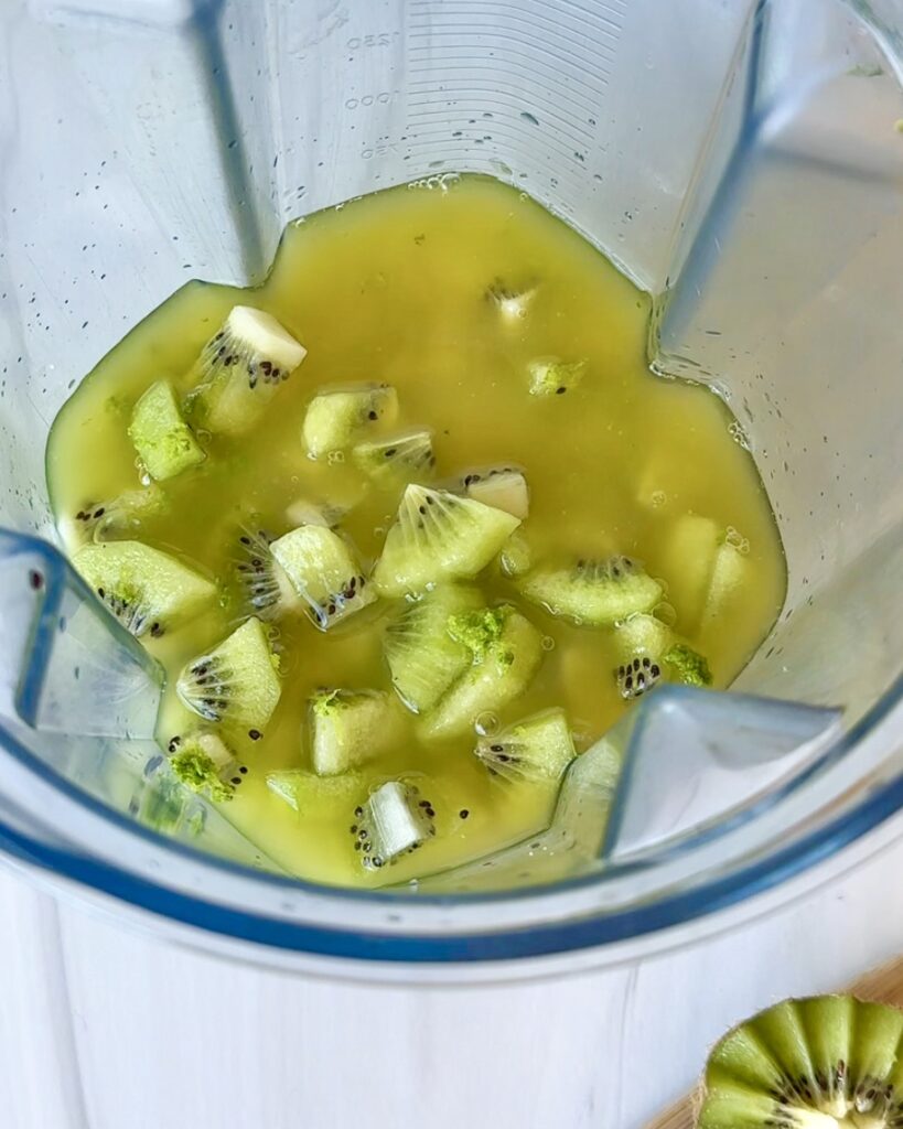 Overhead view of a blender filled with kiwi, pineapple, coconut water, and other ingredients ready to be blended into popsicles.