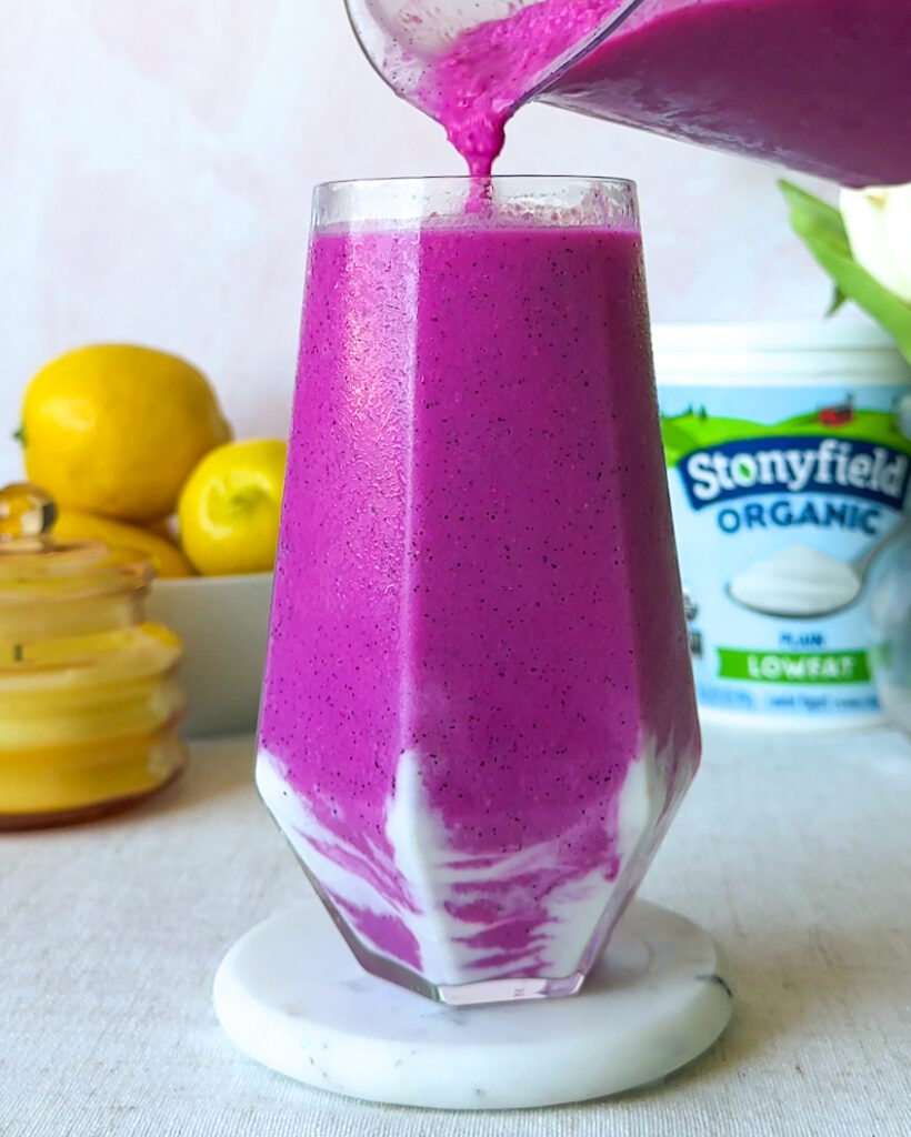 Pouring a vibrant dragon fruit smoothie into a glass with a creamy yogurt swirl