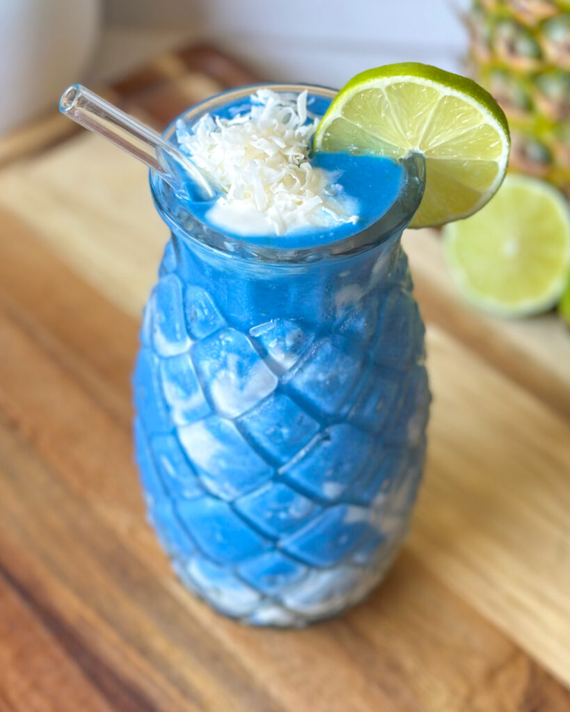 Slightly overhead front on view of pineapple coconut blue spirulina smoothie served in a pineapple shaped glass with a straw