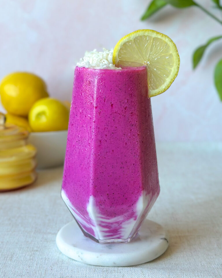 Vibrant pink dragon fruit smoothie with a creamy yogurt swirl, shredded coconut, and fresh lemon garnish