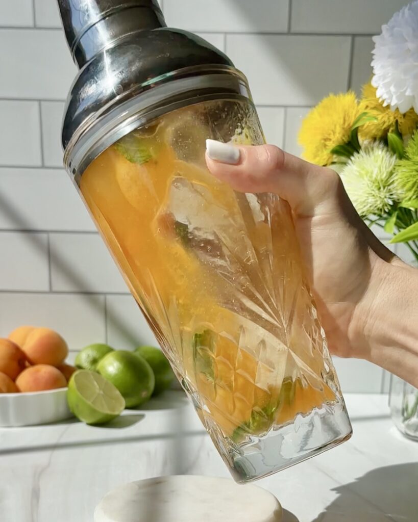 Shaking an apricot mojito in a cocktail shaker with fresh apricots, mint, lime juice, and rum