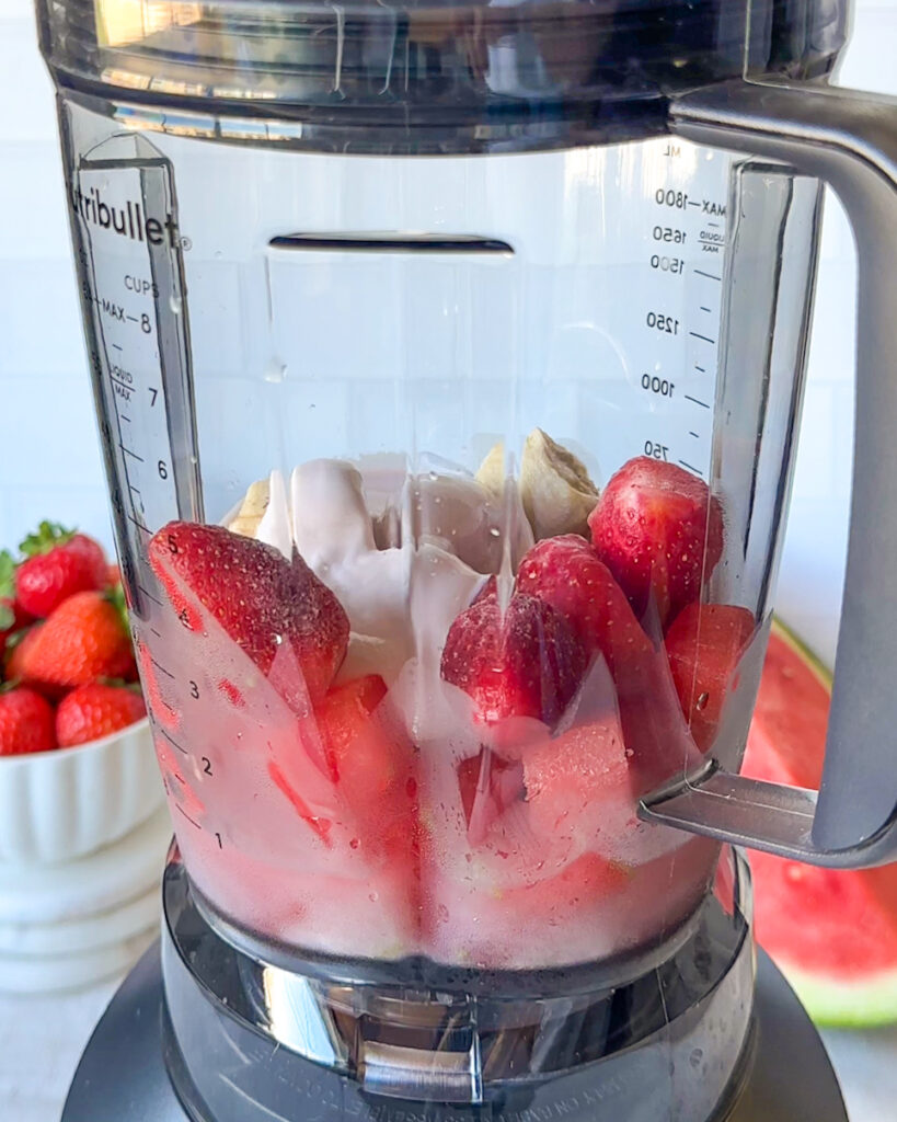 blender full of frozen strawberries, watermelon, yogurt, banana and lime