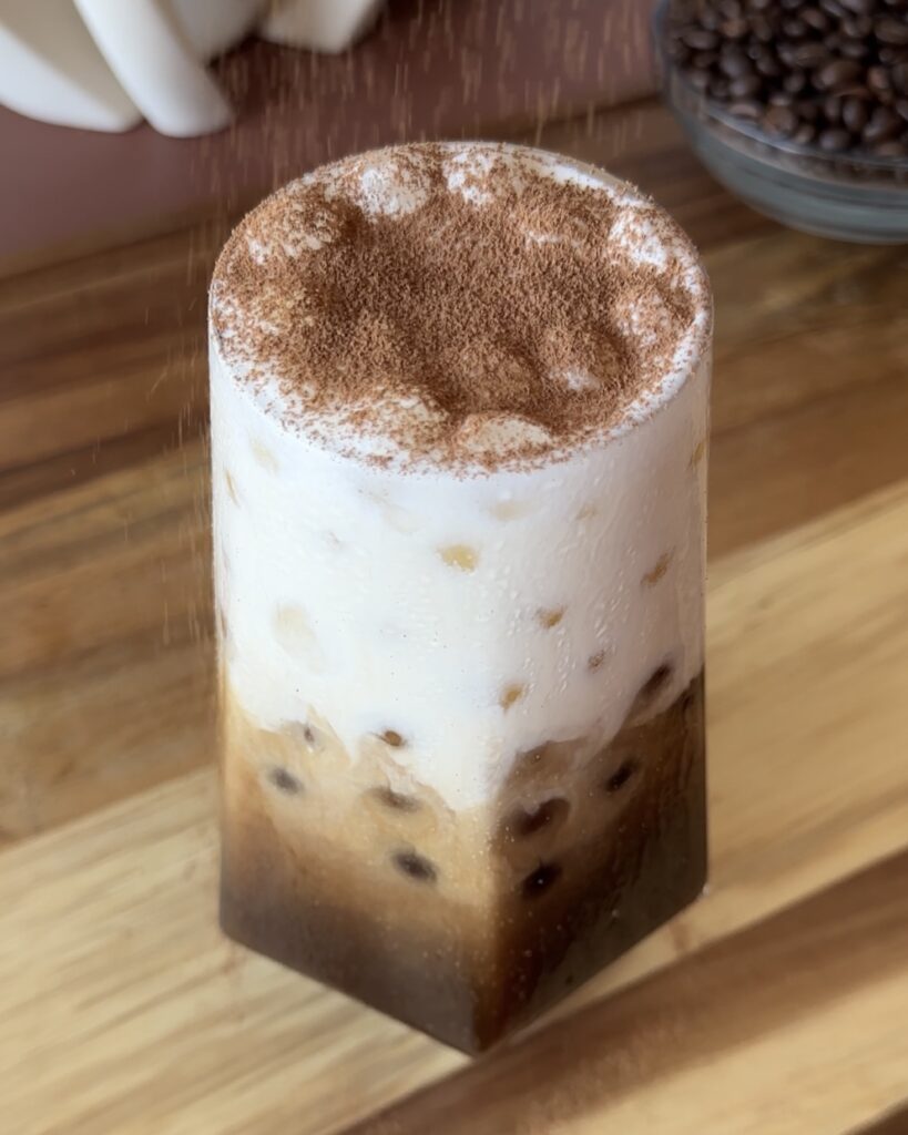 dusting cocoa powder over tiramisu cold brew iced coffee as garnish
