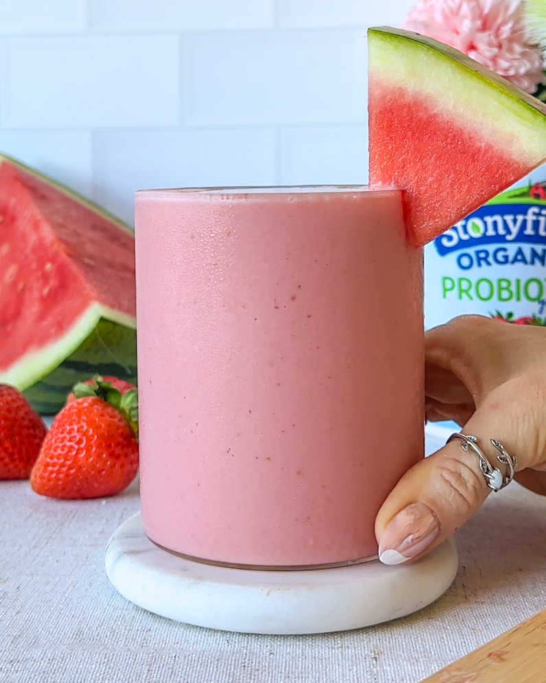 hand holding finished strawberry watermelon smoothie in a chilled glass with watermelon wedge garnish