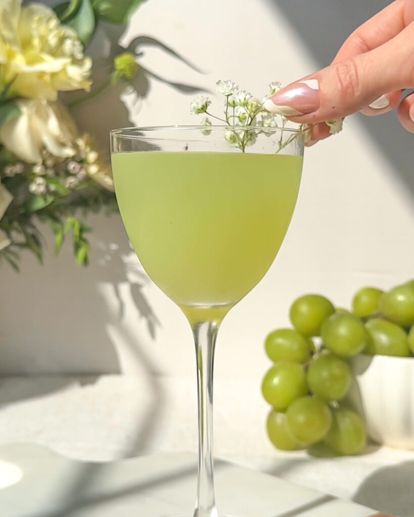 hand placing delicate babys breath florals into finished green grape gimlet cocktail