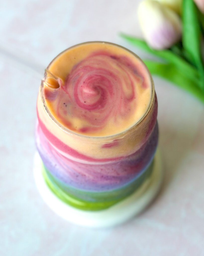 overhead close up of layered rainbow fruit and yogurt smoothie served in a glass with beautiful swirls on top
