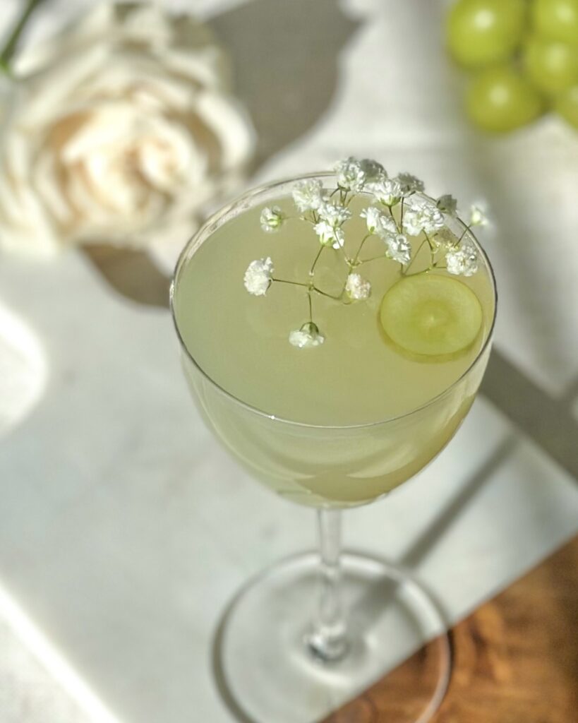 overhead view of finished green grape gimlet cocktail garnished with green grape slice and babys breath florals