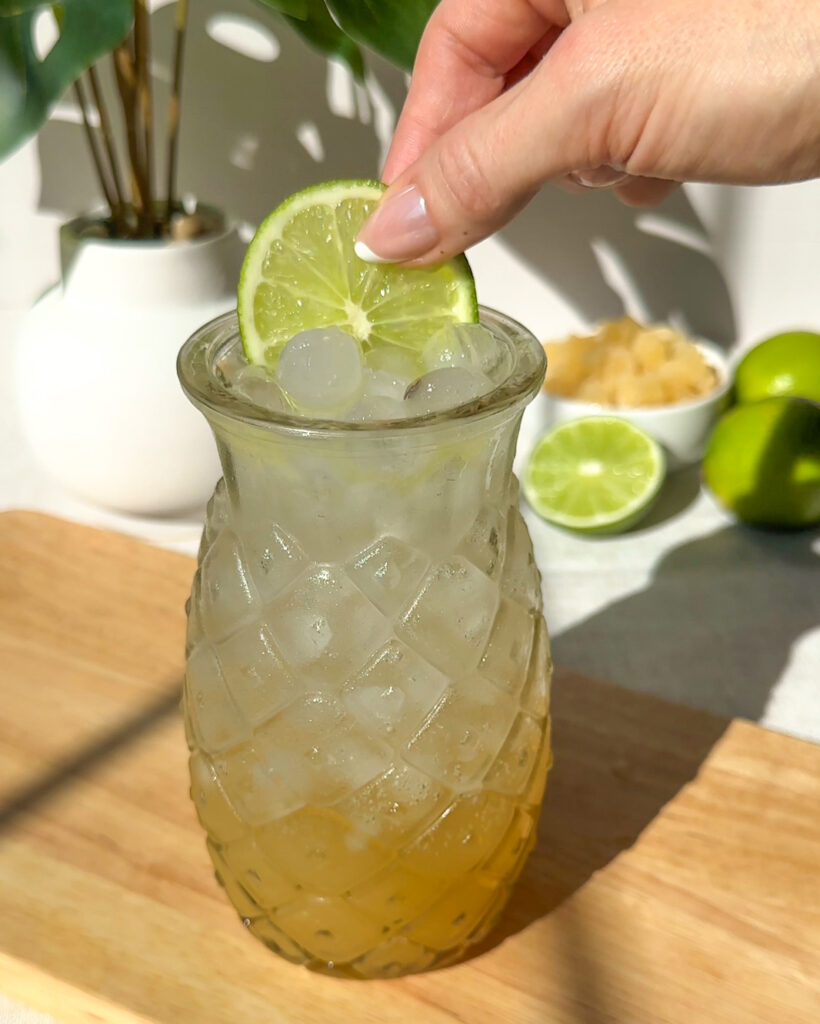 placing a fresh lime wheel as garnish for pineapple rum spritz cocktail recipe