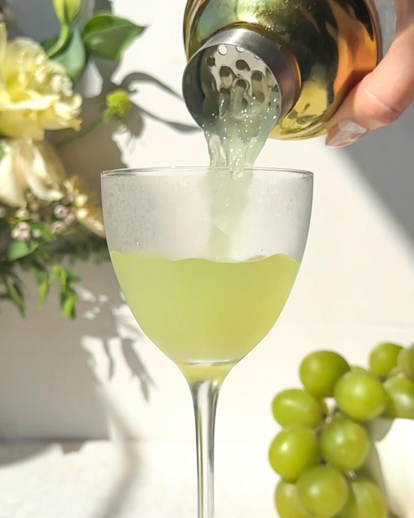 pouring freshly shaken gin green grape gimlet into chilled coupe glass