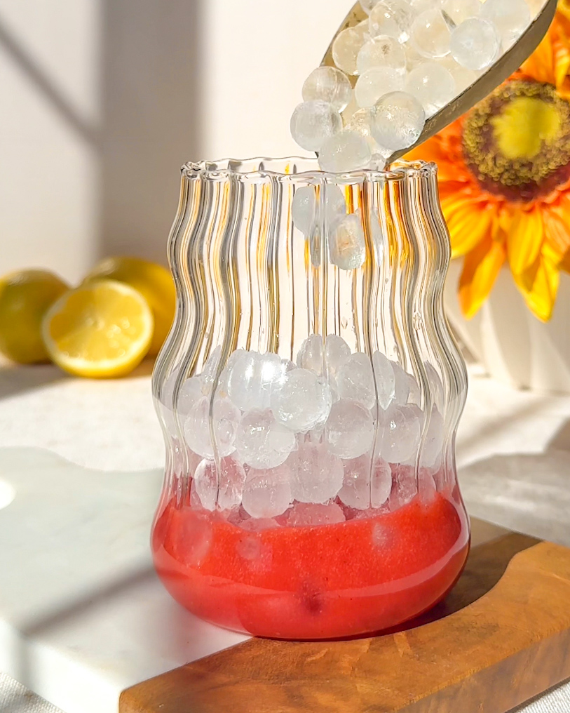 pouring ice cube spheres into glass for5 homemade strawberry electrolyte drink