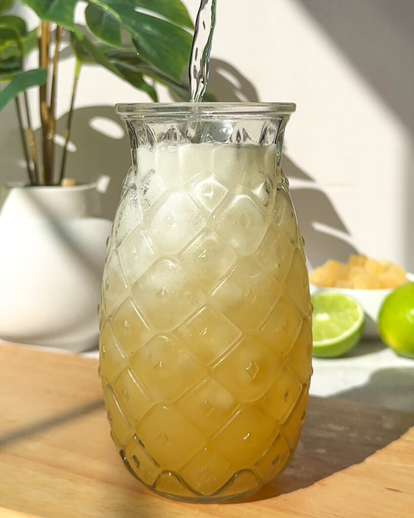 pouring sparkling water into a finished pineapple rum spritz cocktail