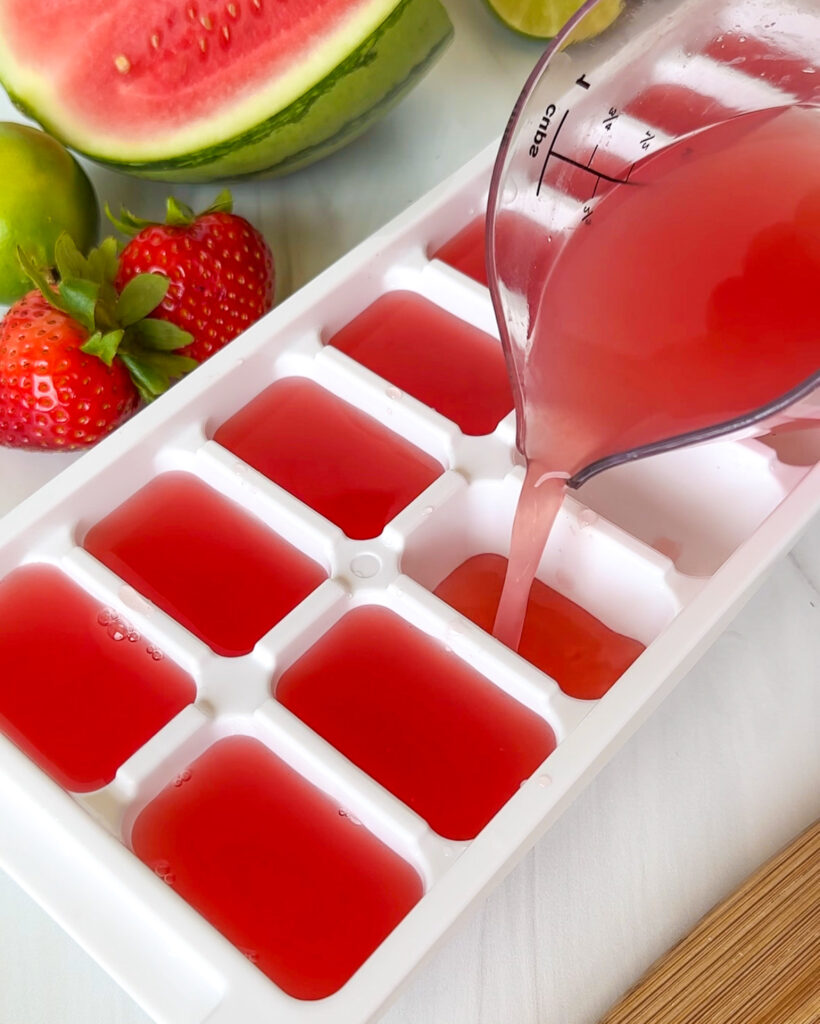 pouring watermelon lime coconut water into ice cube tray for watermelon strawberry ice cubes