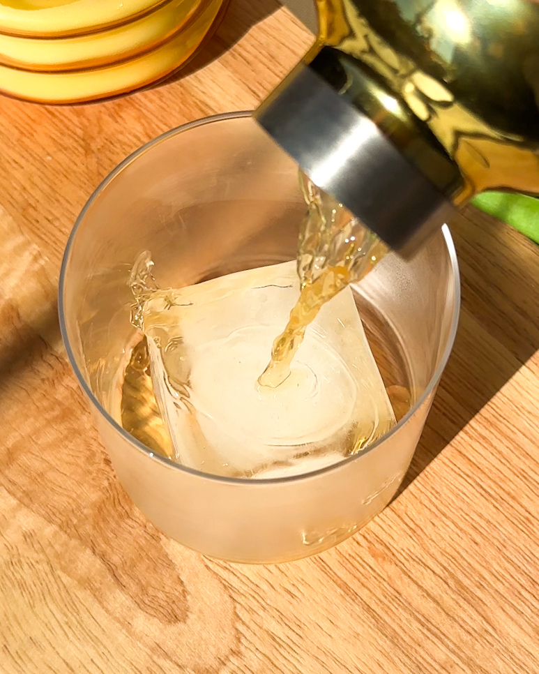 Pouring a Golden Raisin Old Fashioned into a chilled rocks glass over a large ice cube.