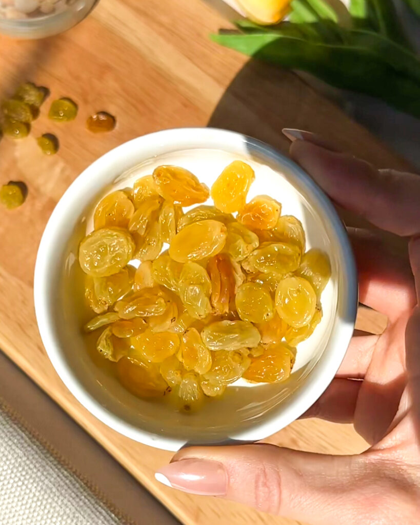 Hand holding a bowl of bourbon-soaked golden raisins used to make a Golden Raisin Old Fashioned.