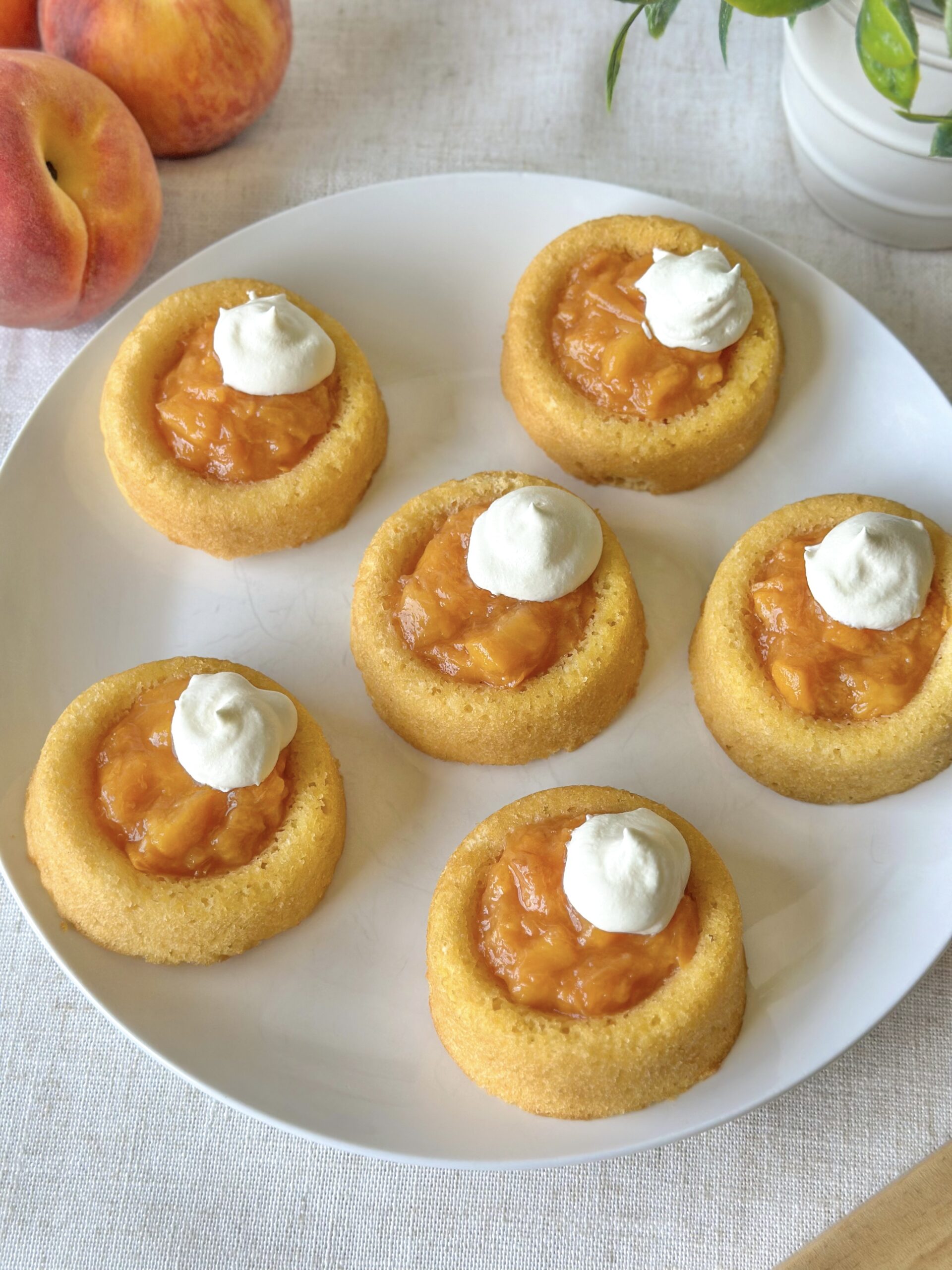 Overhead view of easy peach tarts with fresh peach filling, whipped topping, and ripe peaches in the background.