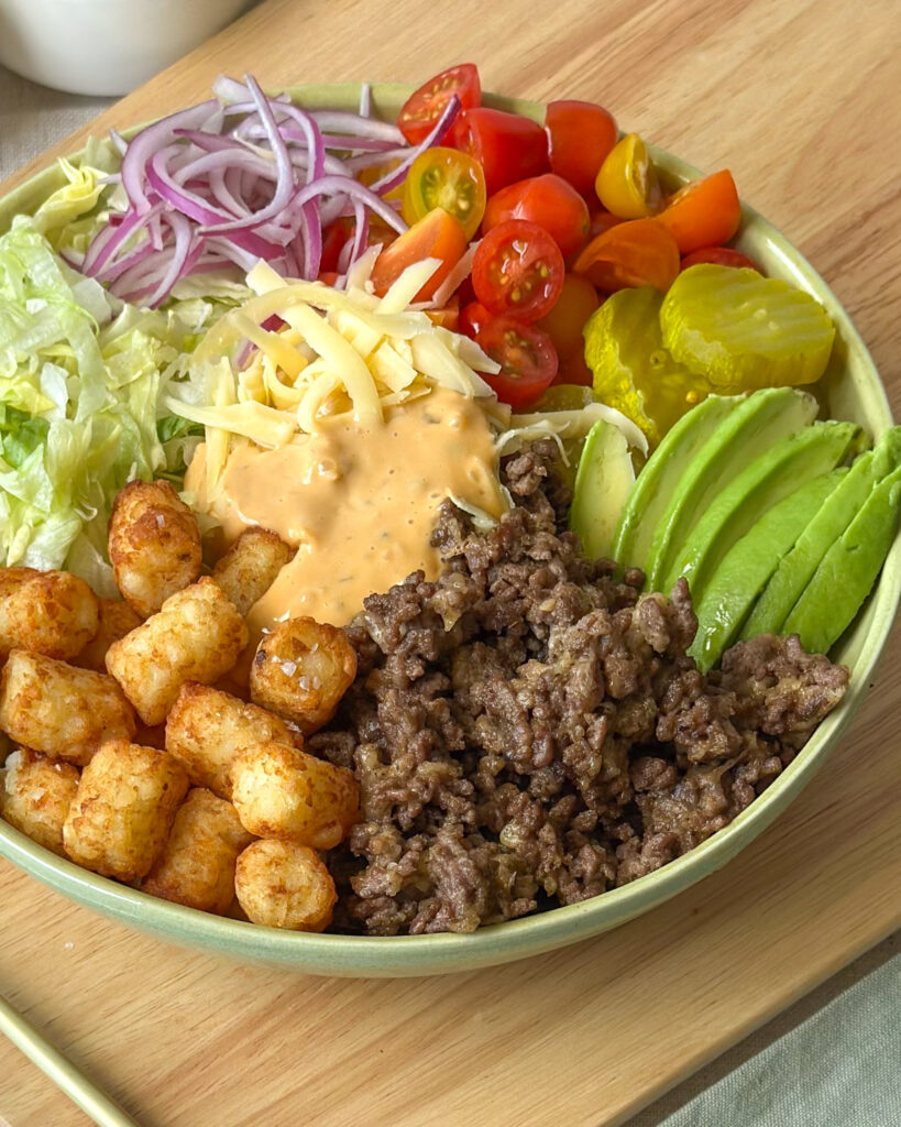 Close-up view of a loaded cheeseburger bowl with crispy tater tots, seasoned beef, vegetables, and special sauce