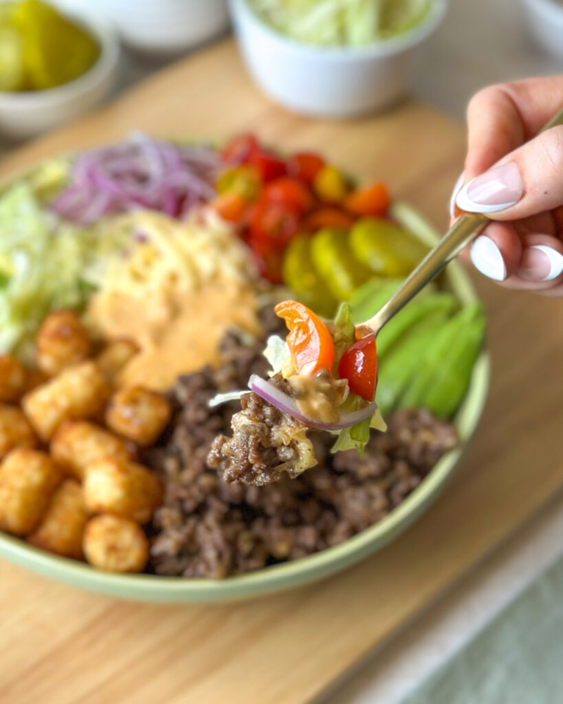 Fork holding a bite of a burger bowl with cheesy beef, vegetables, and toppings