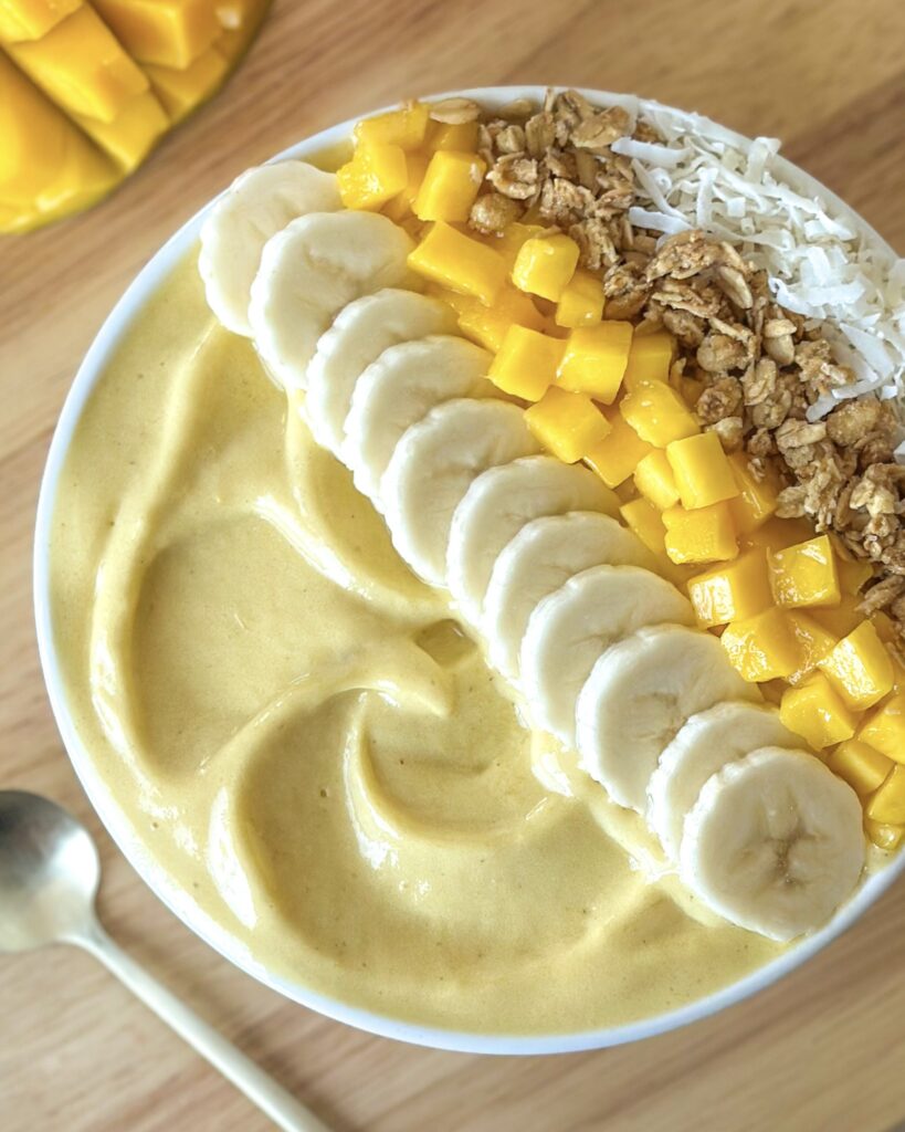 Close-up overhead view of a creamy mango smoothie bowl topped with fresh fruit, granola, and coconut