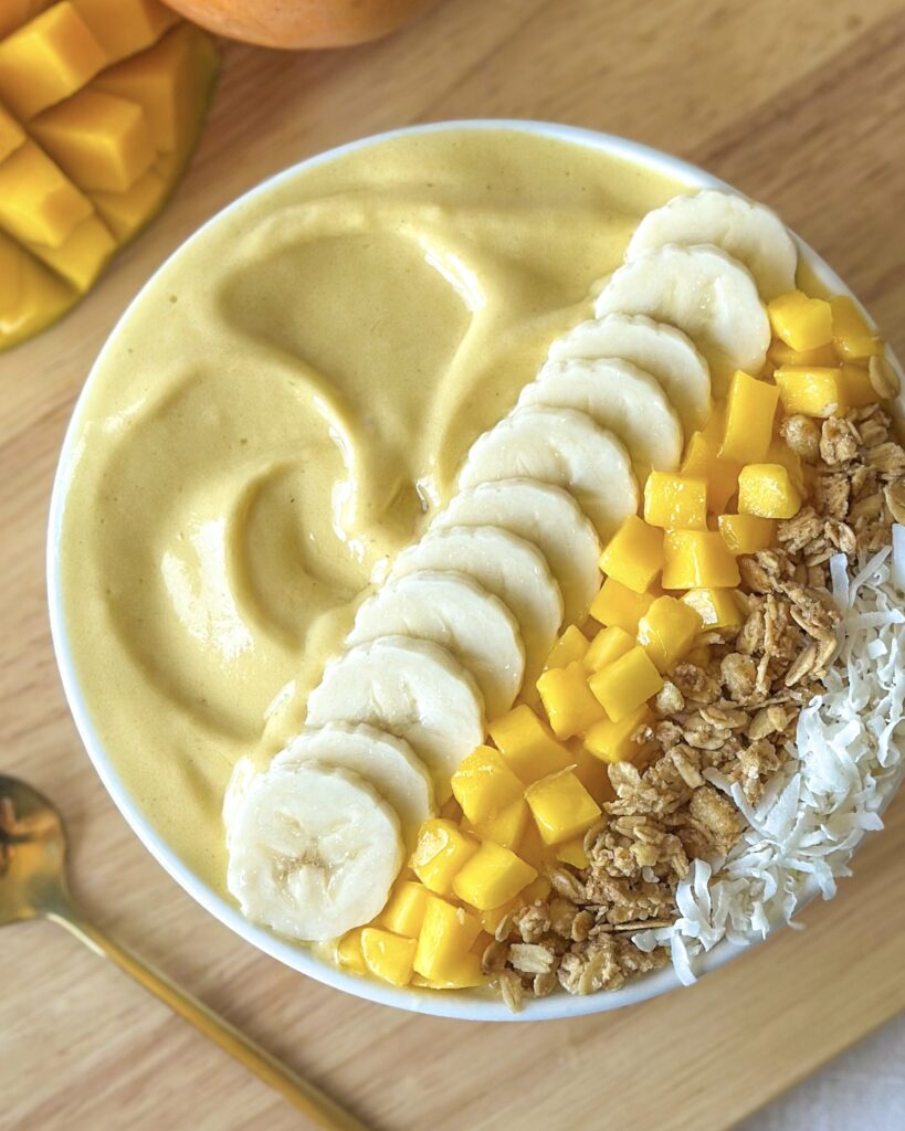 Close-up overhead view of a creamy thick mango smoothie bowl topped with fresh mango, granola, and coconut