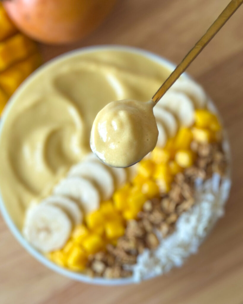 Spoon holding a scoop of thick mango smoothie in front of a softly blurred smoothie bowl