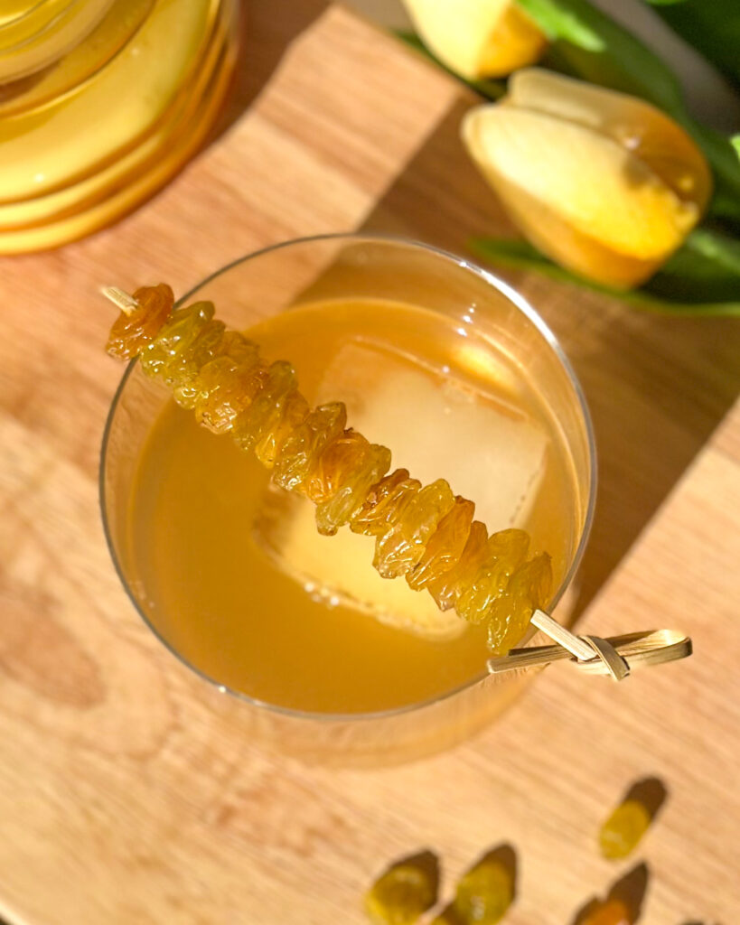 Overhead view of a Golden Raisin Old Fashioned with a row of bourbon-soaked golden raisins resting across the rim of the glass.