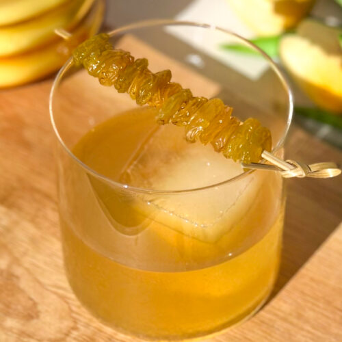 Golden Raisin Old Fashioned cocktail garnished with bourbon-soaked golden raisins on a cocktail pick.