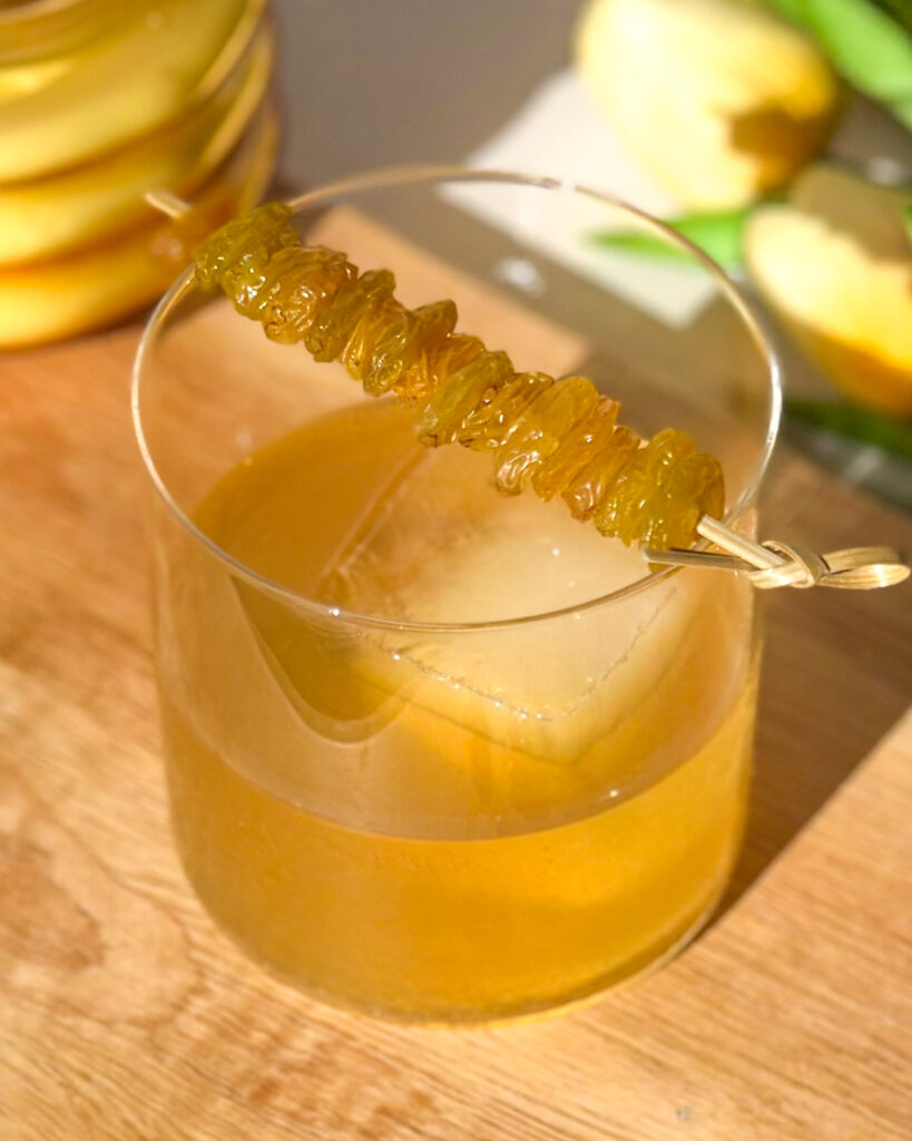 Golden Raisin Old Fashioned cocktail garnished with bourbon-soaked golden raisins on a cocktail pick.