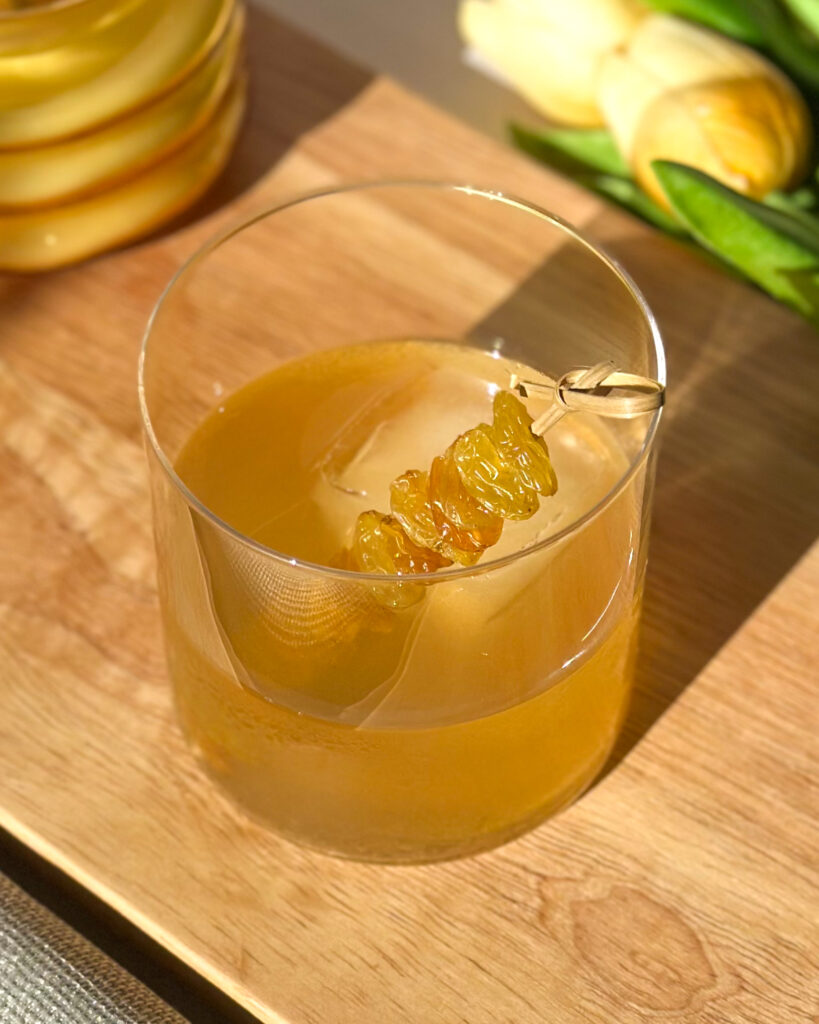 Golden Raisin Old Fashioned cocktail garnished with bourbon-soaked golden raisins on a cocktail pick
