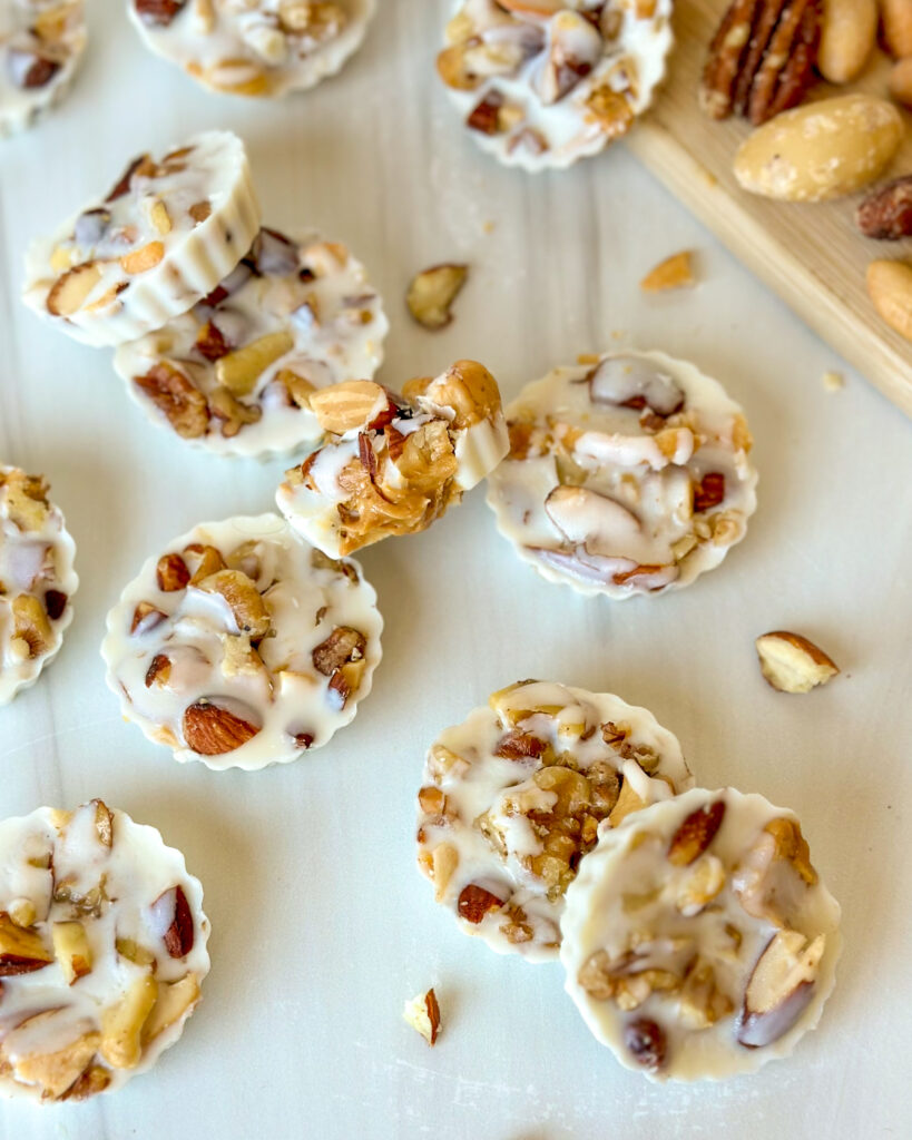 Overhead view of white chocolate peanut butter cups scattered around a scene with one bitten open to show the creamy peanut butter center and mixed nuts in the background