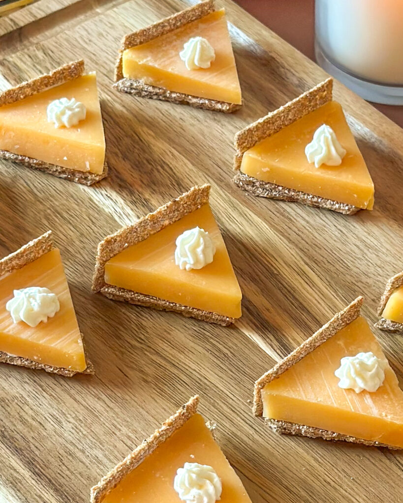 Pumpkin pie cheese and cracker bites arranged on a wooden cutting board