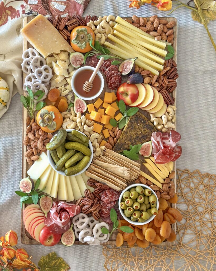 Overhead view of a fall charcuterie board surrounded by seasonal ingredients and serving dishes