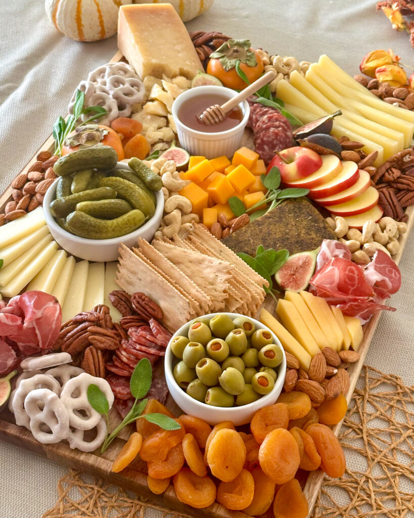 Front view of a colorful fall charcuterie board arranged with seasonal fruit, cheeses, cured meats, nuts, and crackers