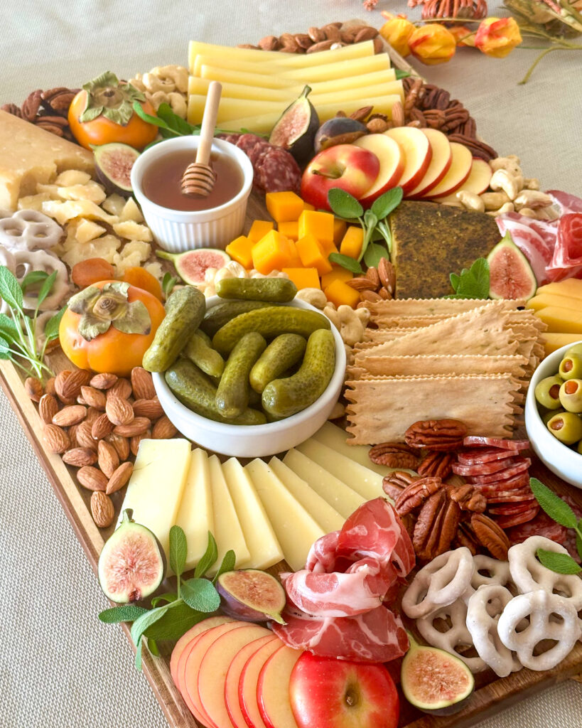 Front view of an abundant fall charcuterie board filled with cheeses, meats, fruit, nuts, crackers, and other snacks