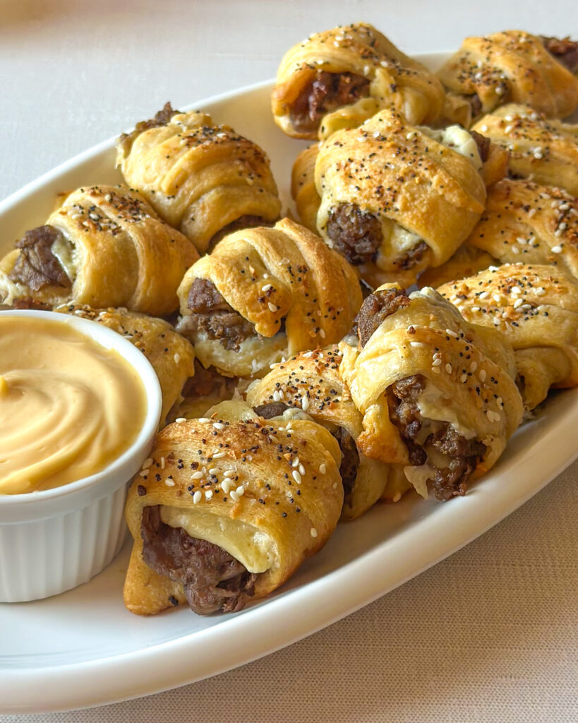 Golden cheesy steak crescent roll bites arranged on a serving platter with dipping sauce