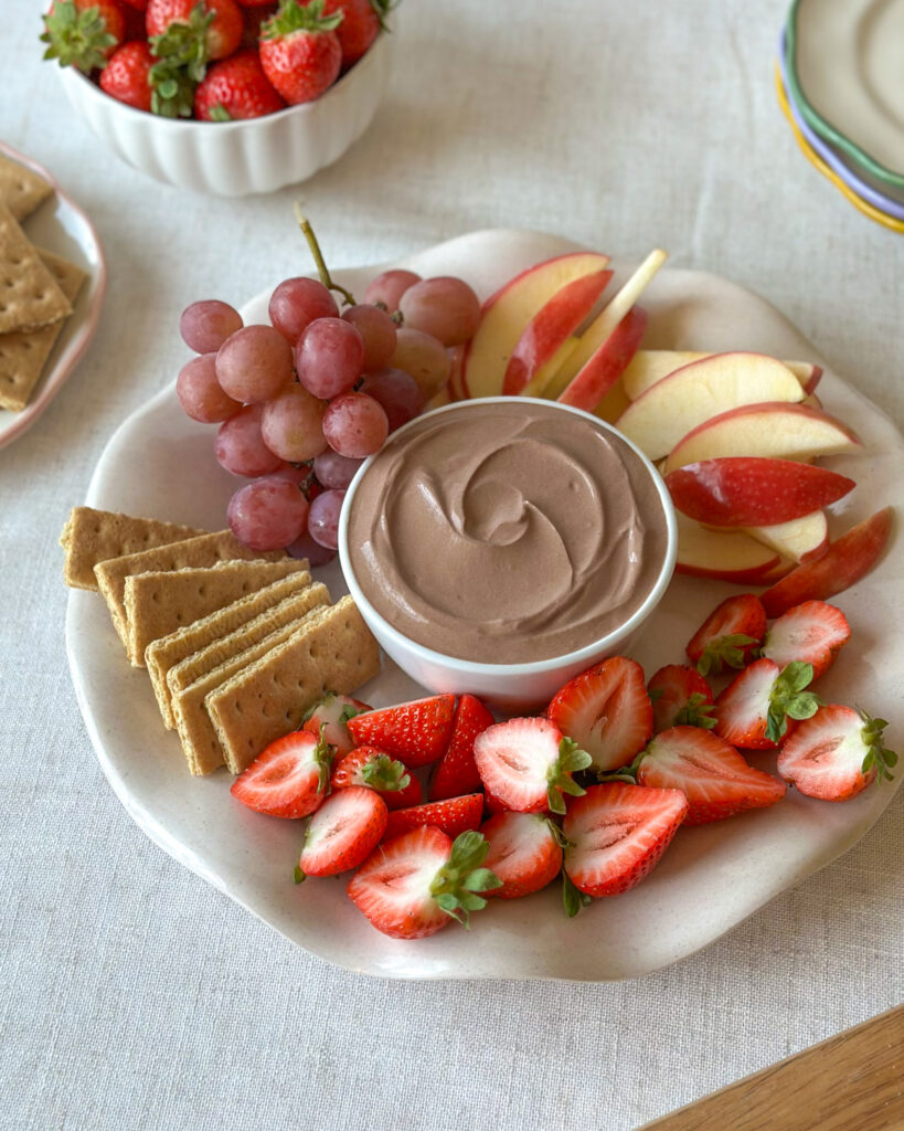 Overhead view of a high-protein chocolate dip platter with strawberries, apple slices, grapes, and graham crackers